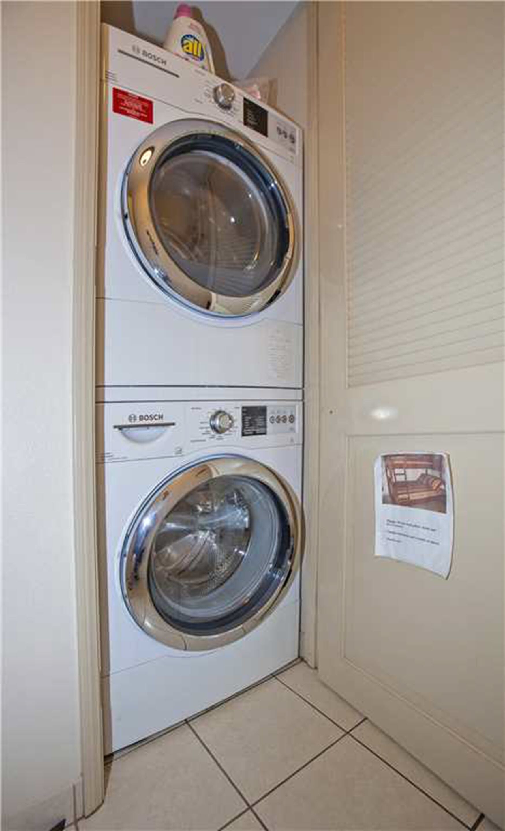 A Bosch washing machine in a laundry room with a tiled floor and a notice on the wall.