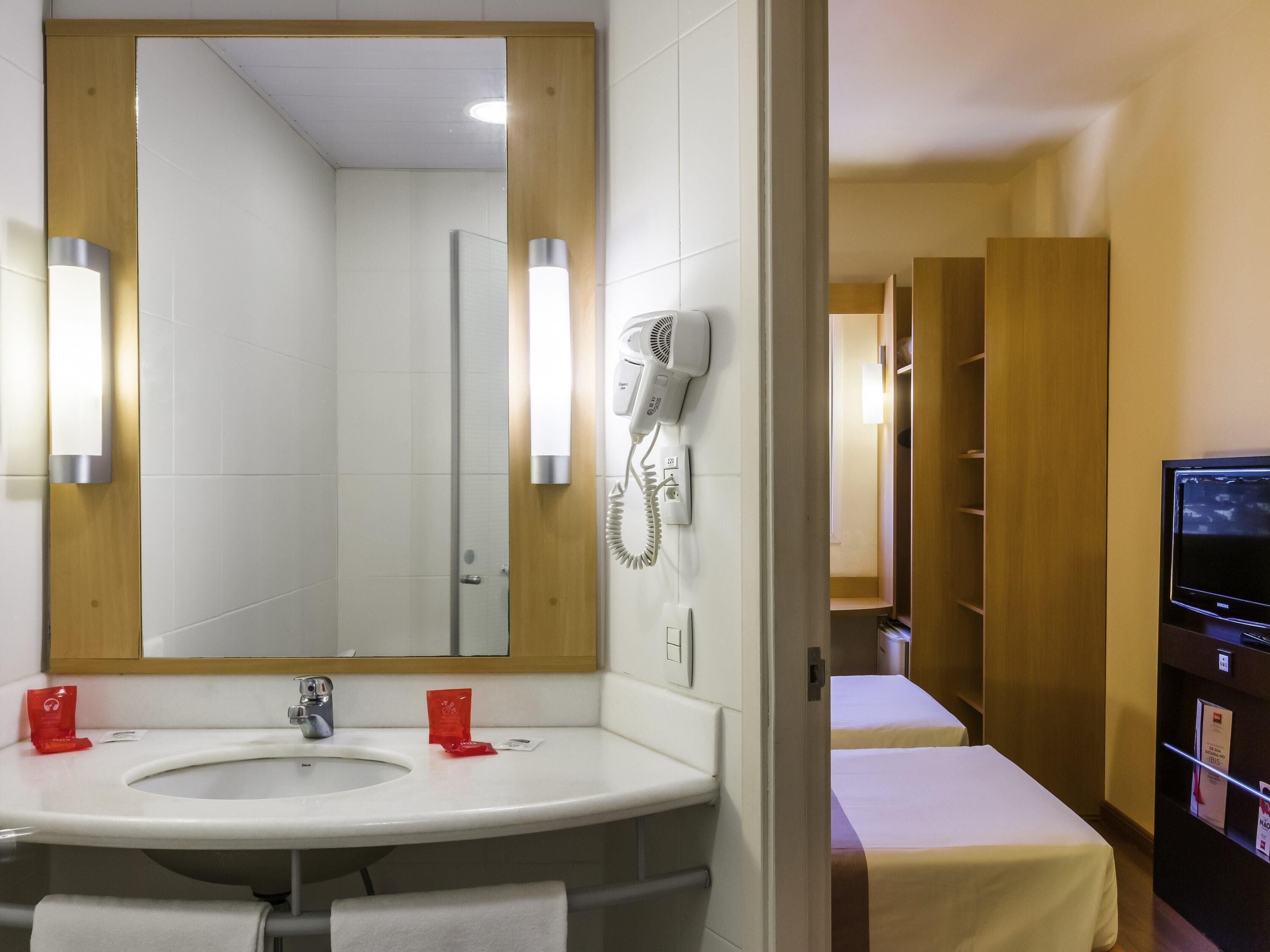 A hotel bathroom with a sink, mirror, hairdryer, and towel rack.
