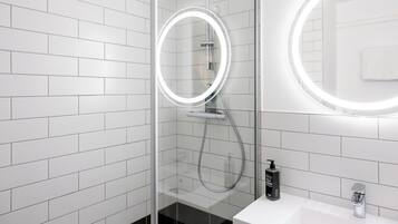A modern bathroom with white subway tiles, a glass-enclosed shower with a handheld showerhead, and a round mirror with a lighted frame.