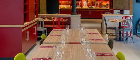 A restaurant with a long wooden table set for a meal, red chairs, and a counter with a display of food items.