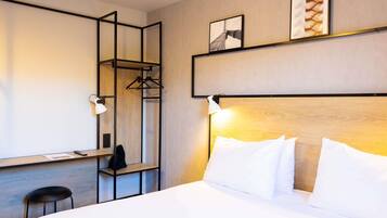 A hotel room with a bed, a desk, a chair, a coat rack, and two wall-mounted lamps.