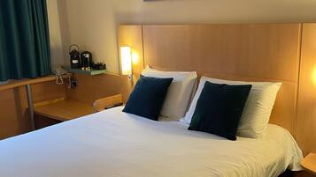 A hotel room with a large bed, a desk with a phone, a coffee maker, and a wall-mounted lamp.