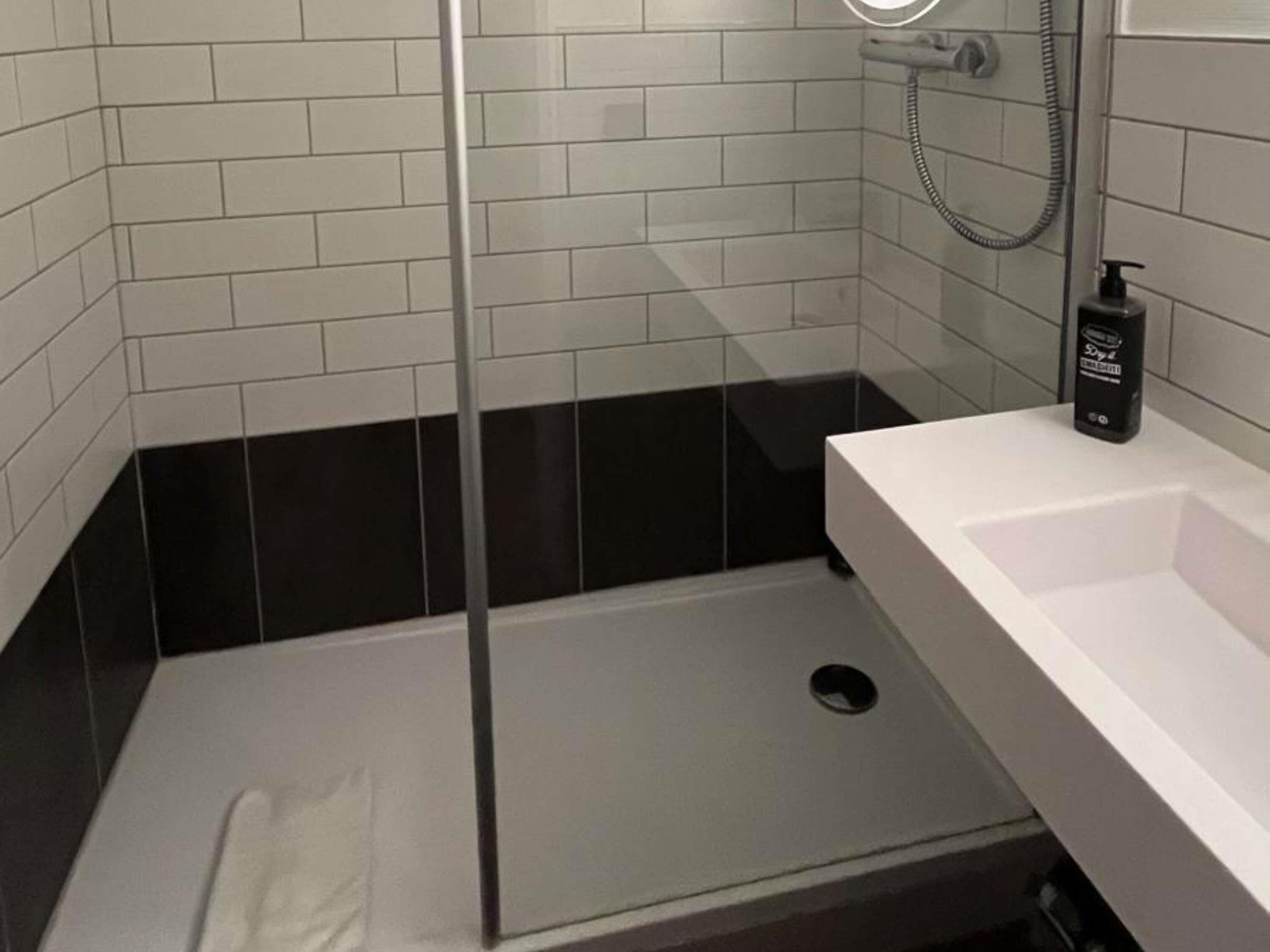 Un baño moderno con cabina de ducha de vidrio, un lavamanos blanco y un dispensador de jabón negro.