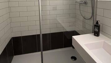 Un baño moderno con cabina de ducha de vidrio, un lavamanos blanco y un dispensador de jabón negro.