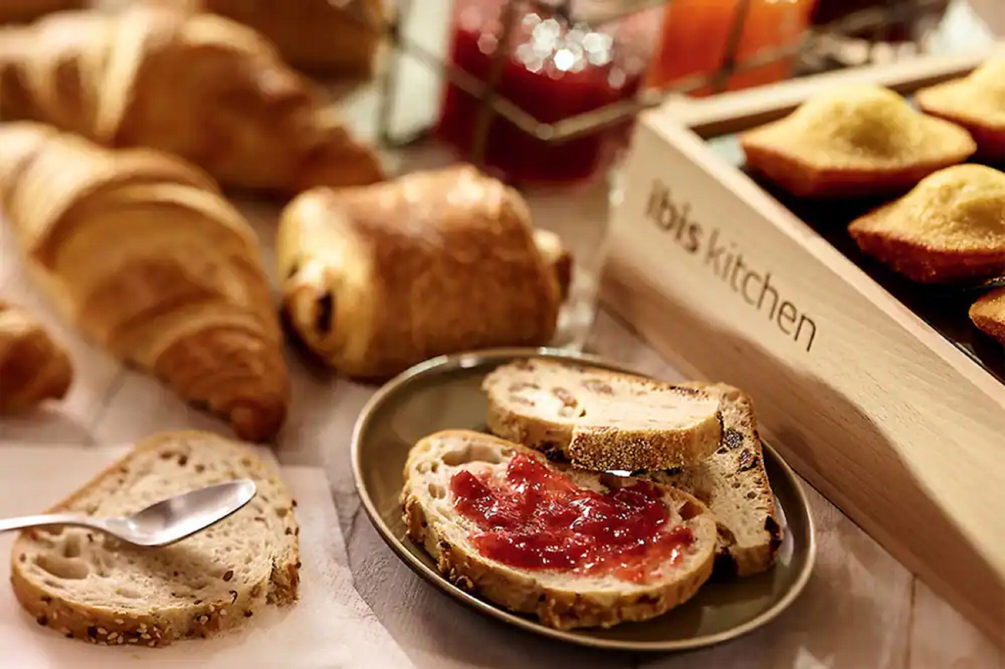 A variety of bread and pastries, including croissants and sliced bread with jam, on a table.