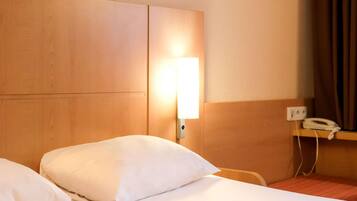 Quarto de hotel com cabeceira de madeira, luminária de mesa, telefone e cama com roupa de cama branca.