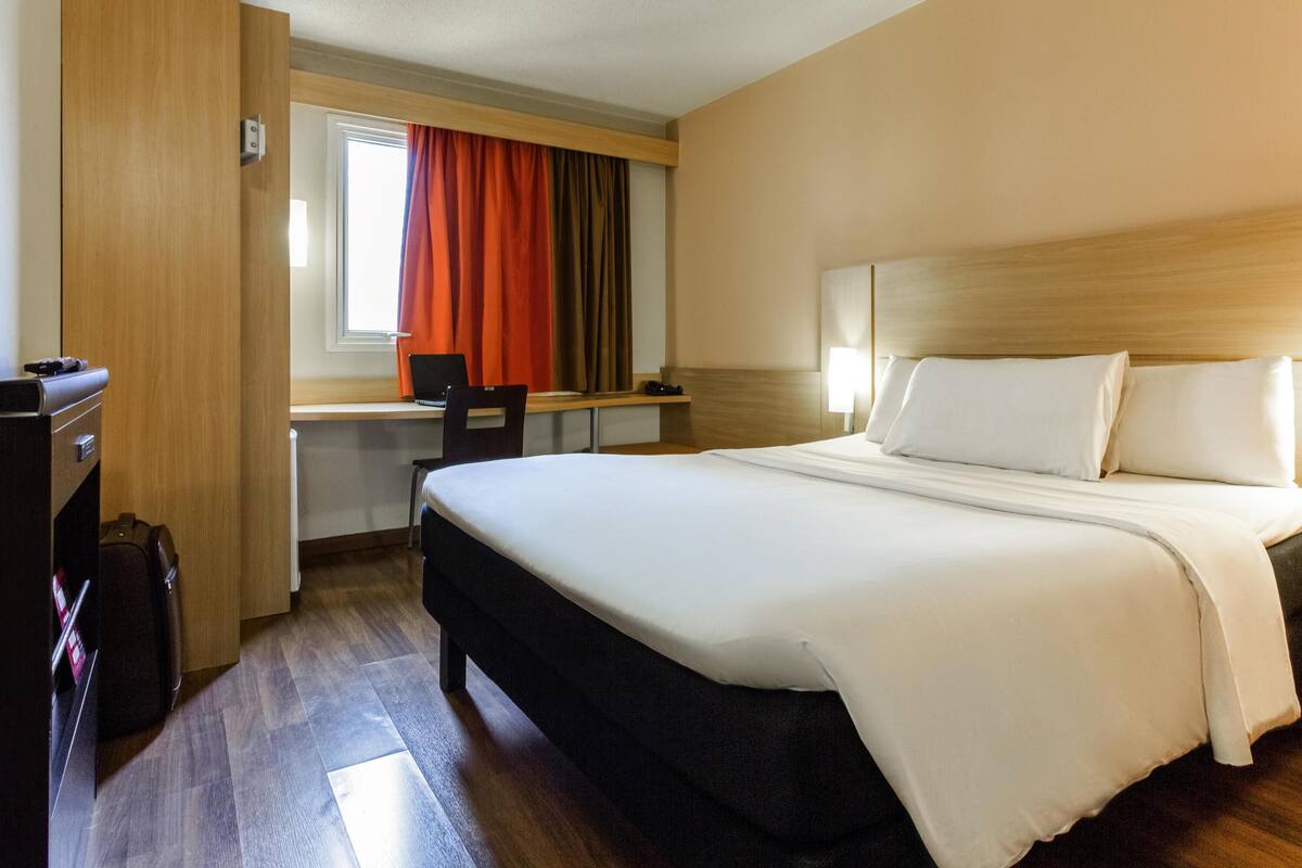Una habitación de hotel con cama, escritorio, silla y maleta.