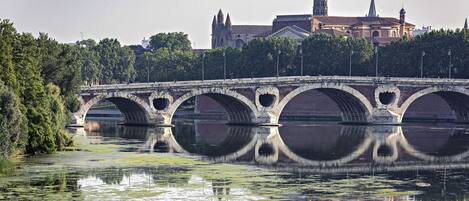 A stone bridge with multiple arches over a calm river, reflecting the surrounding trees and buildings.