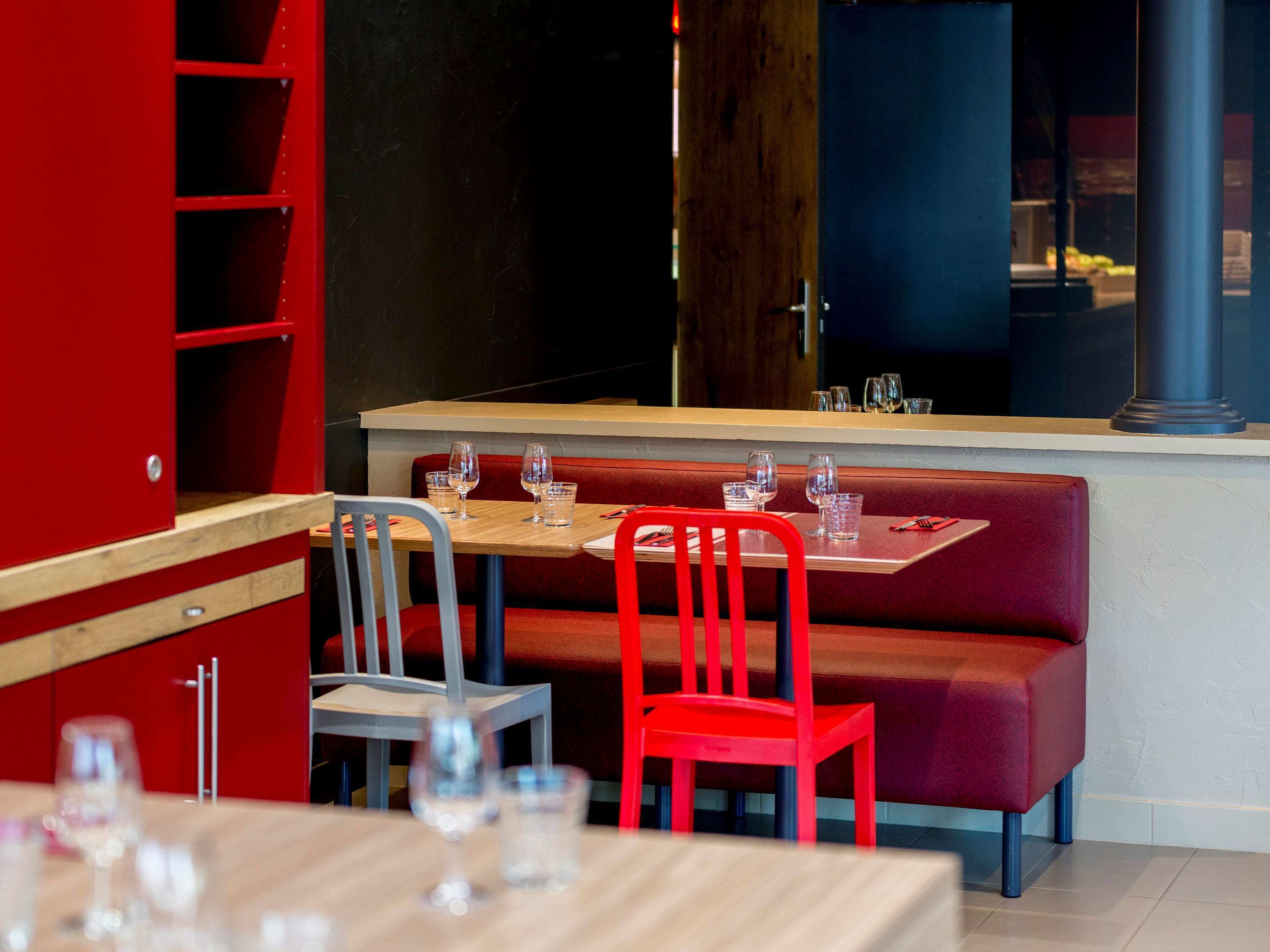 Ein Restaurantinneres mit roten Sitzbänken, Holztischen und Metallstühlen.