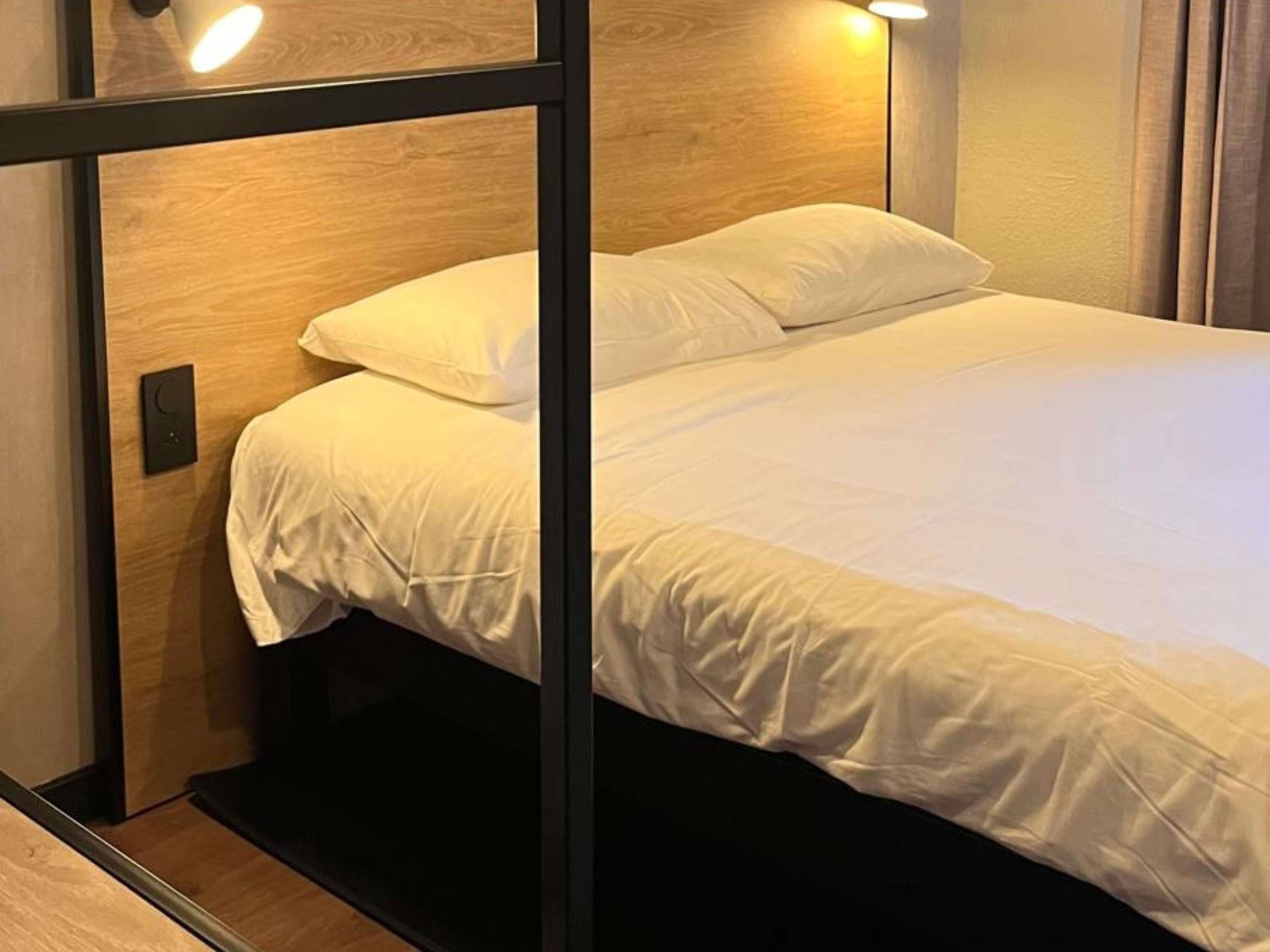 A neatly made bed with white linens, a wooden headboard, and a black frame.