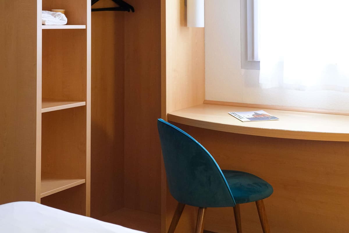 Una habitación con cama, escritorio, silla, ventana y armario.