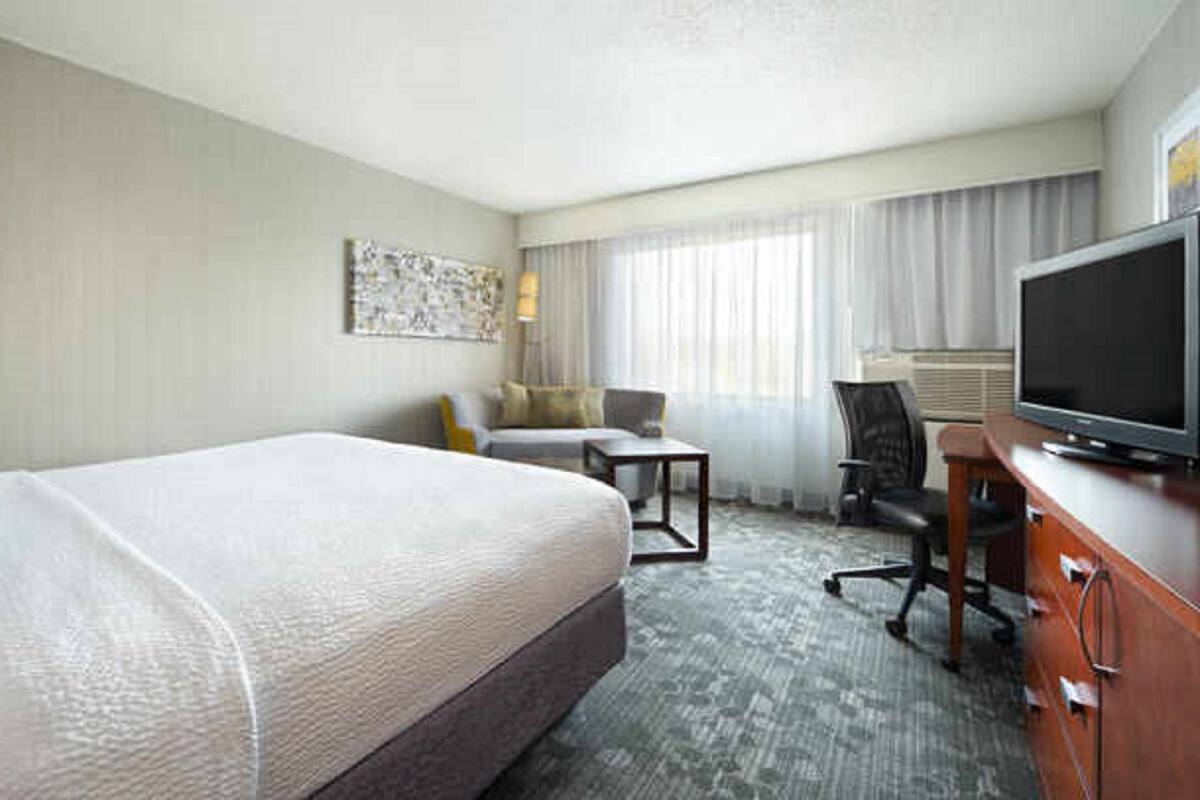 A hotel room with a bed, a desk, a chair, a television, and a window with curtains.