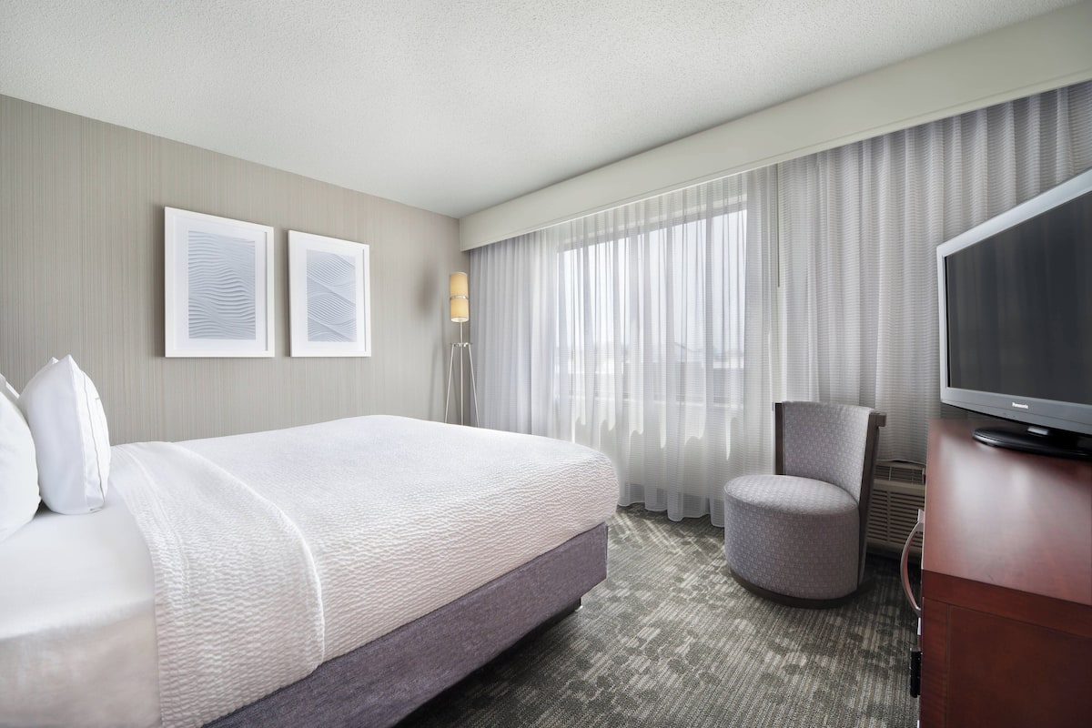 A hotel room with a large bed, a television, a chair, and two framed pictures on the wall.
