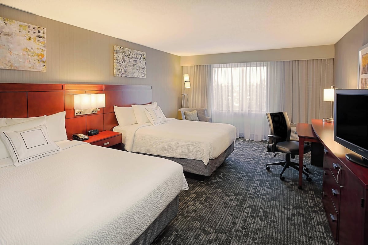 A hotel room with two beds, a desk with a TV, a chair, and artwork on the walls.