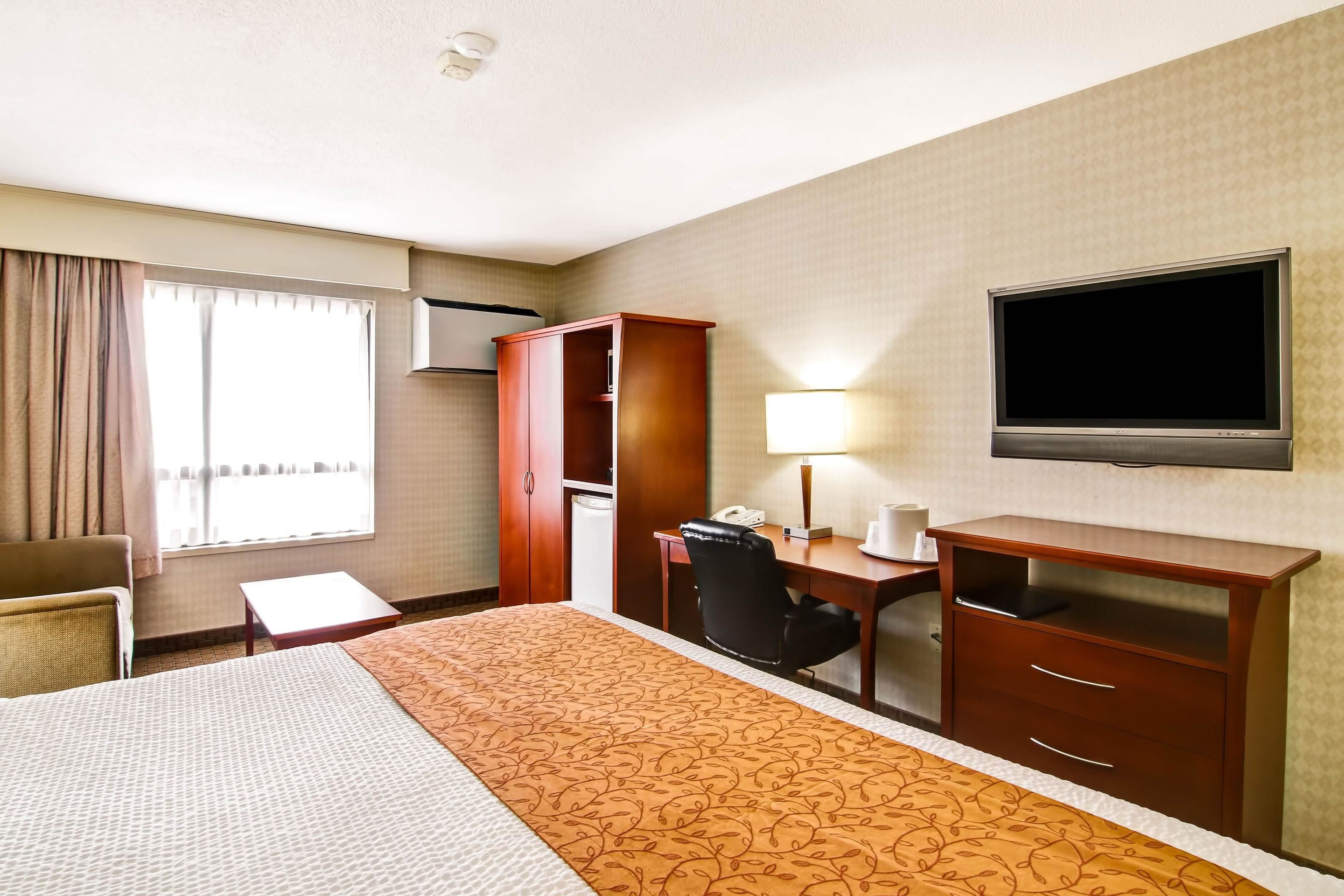 A hotel room with a bed, a desk, a chair, a television, and a wardrobe.