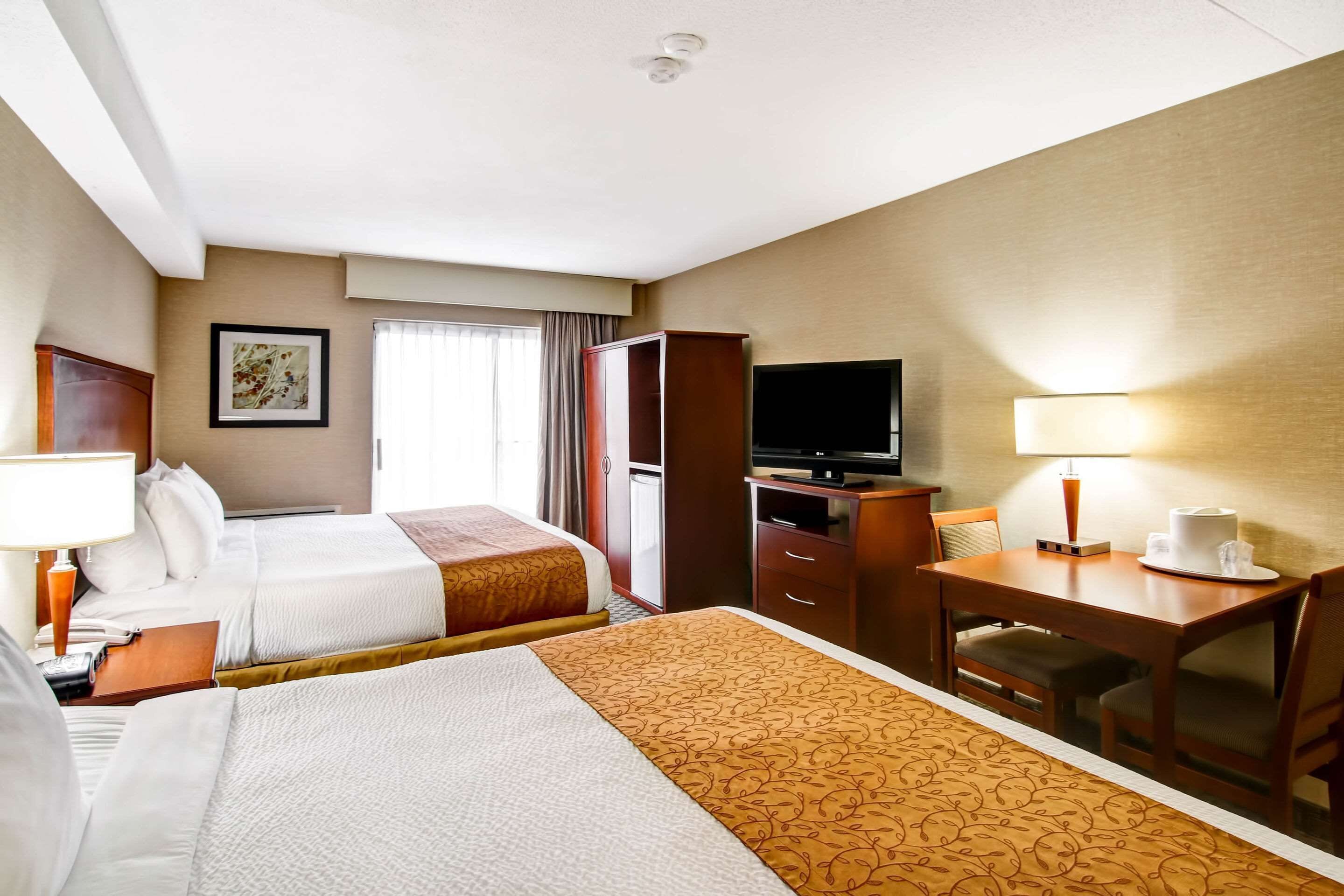 Quarto de hotel com duas camas, uma escrivaninha com televisão, luminária e cafeteira.