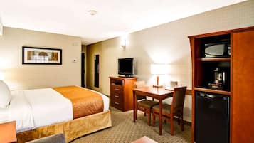 A hotel room with a bed, desk, chair, television, and a refrigerator.