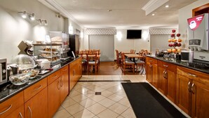 A modern kitchen with wooden cabinets, a dining area with chairs, a coffee machine, and a flat-screen TV on the wall. - Quality Inn (Kitchener)
