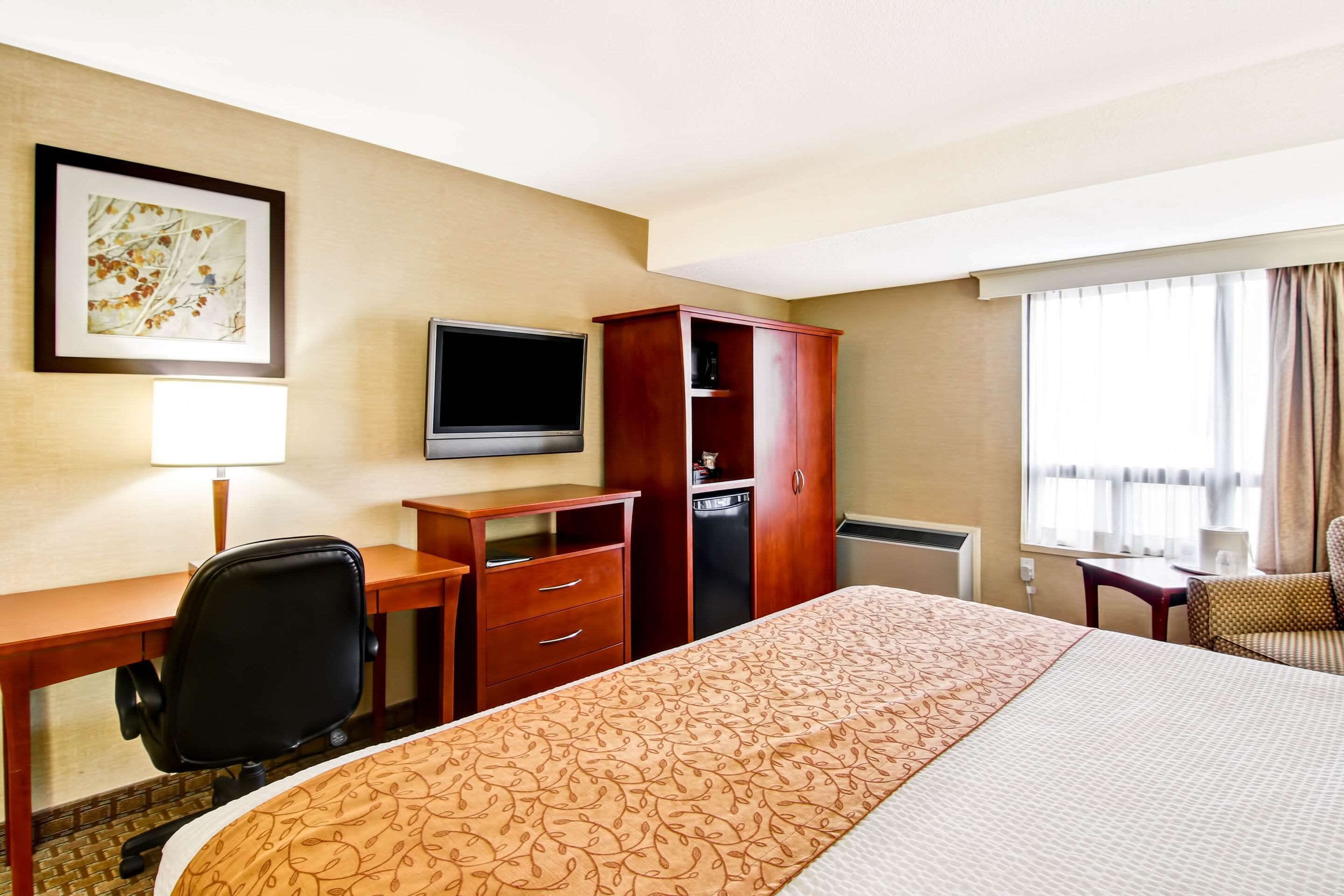 A hotel room with a large bed, a desk with a chair, a television, a wardrobe, and a window with curtains.