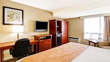 A hotel room with a large bed, a desk with a chair, a television, a wardrobe, and a window with curtains.