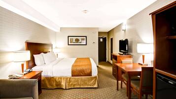 A hotel room with a bed, bedside table with a lamp, a desk with a chair, a television, and a wardrobe.