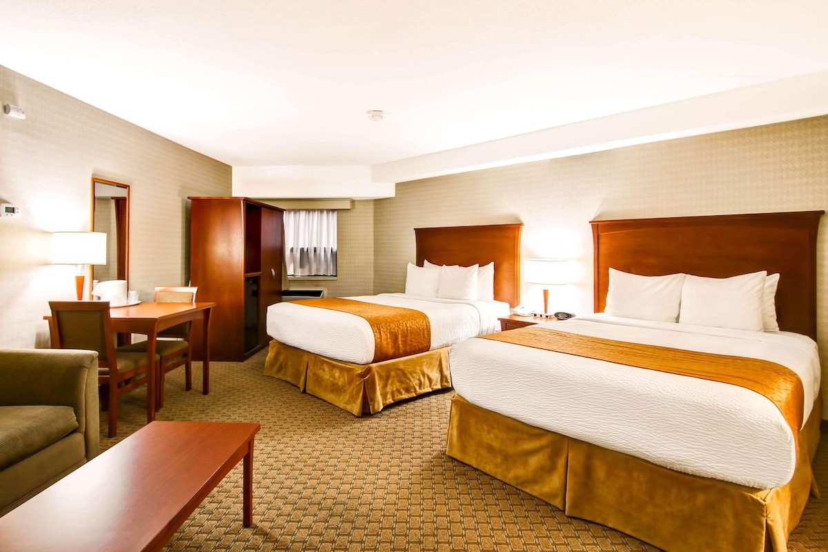 A hotel room with two beds, a desk, a chair, and a small table.