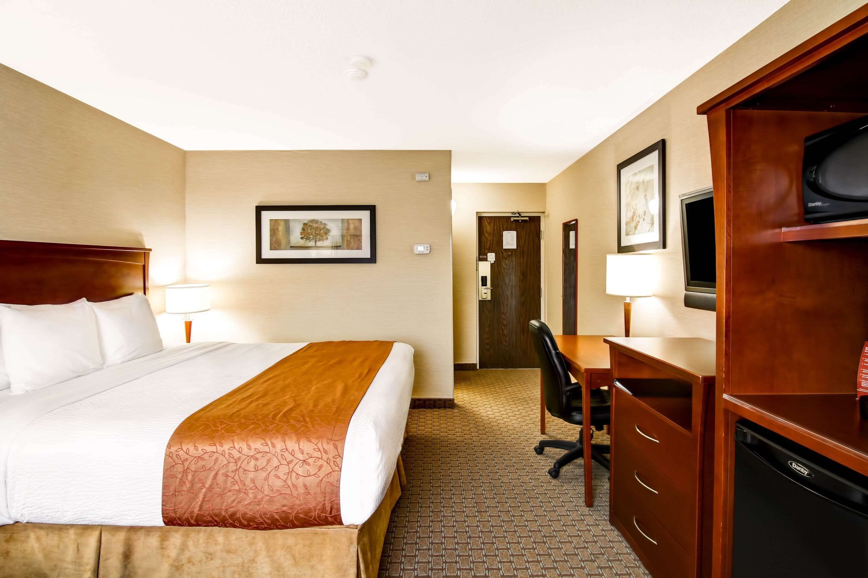 A hotel room with a large bed, a desk with a chair, a television, and a minibar.
