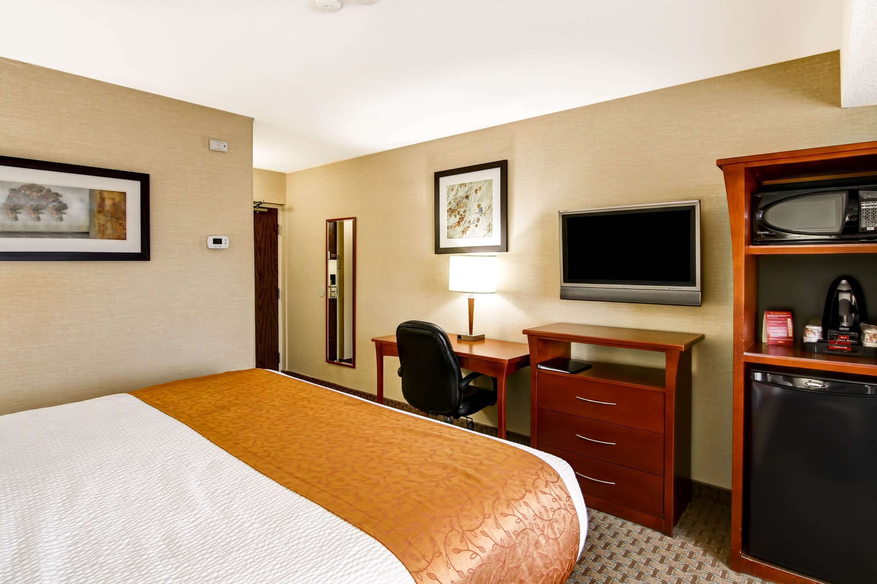 Una habitación de hotel con una cama, un escritorio con silla, televisión, microondas y refrigerador.
