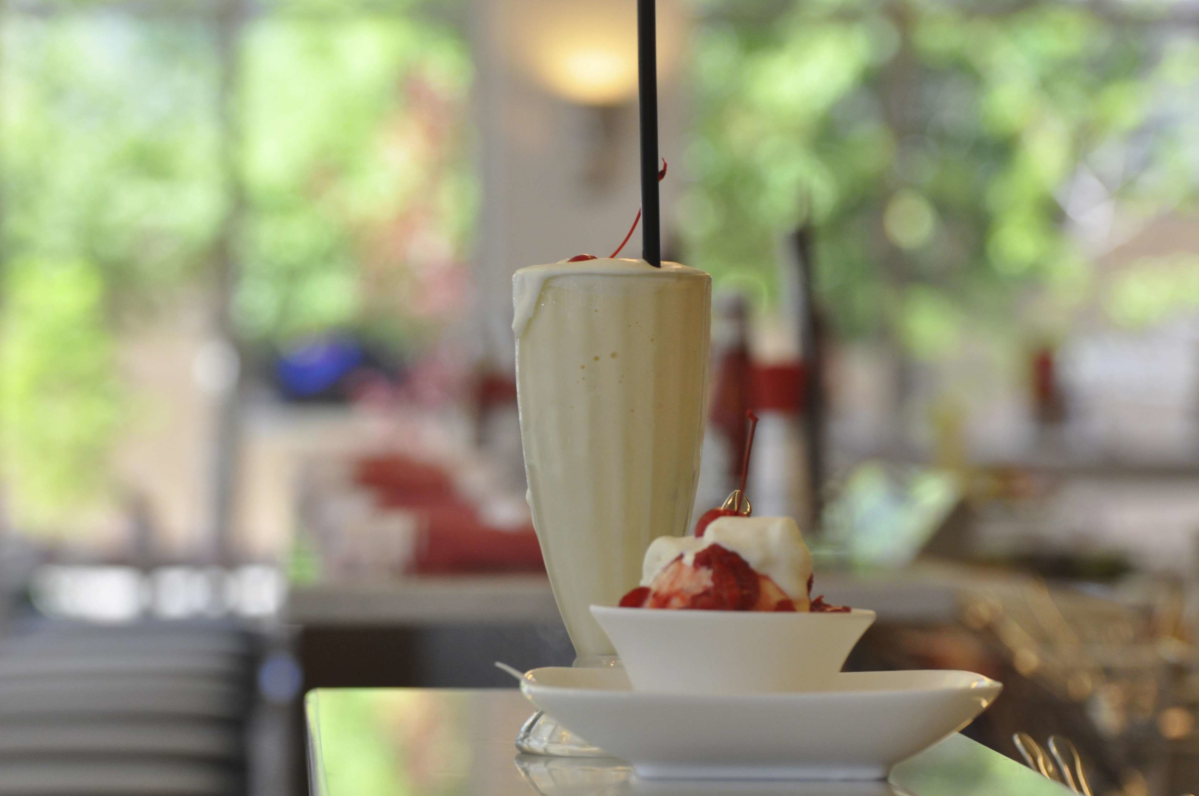 Un dessert servi dans un grand verre et accompagné d’un petit bol, le tout posé sur une table.