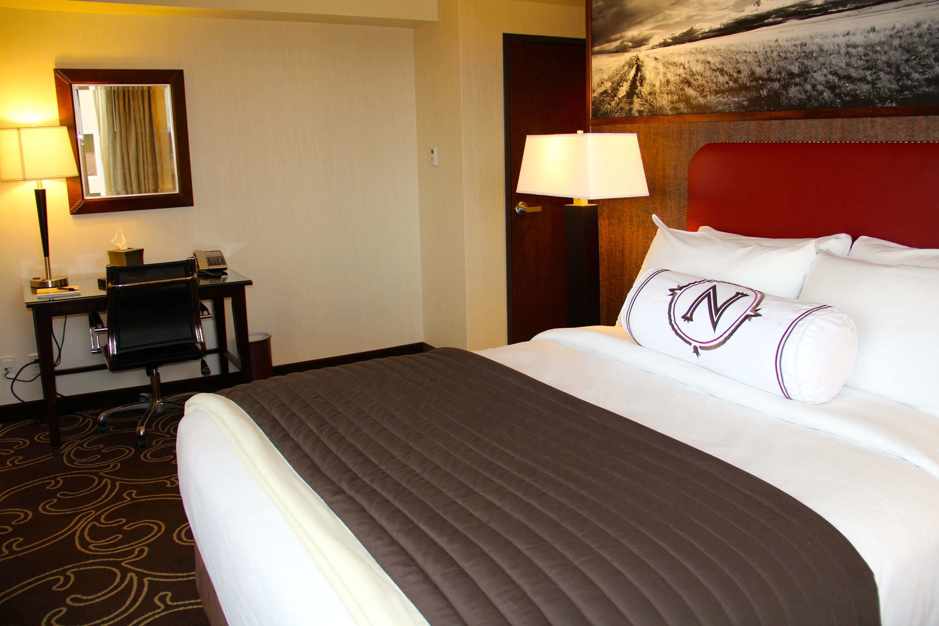A hotel room with a large bed, a desk with a chair, a lamp, and a painting on the wall.