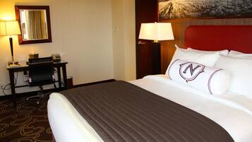 A hotel room with a large bed, a desk with a chair, a lamp, and a painting on the wall.