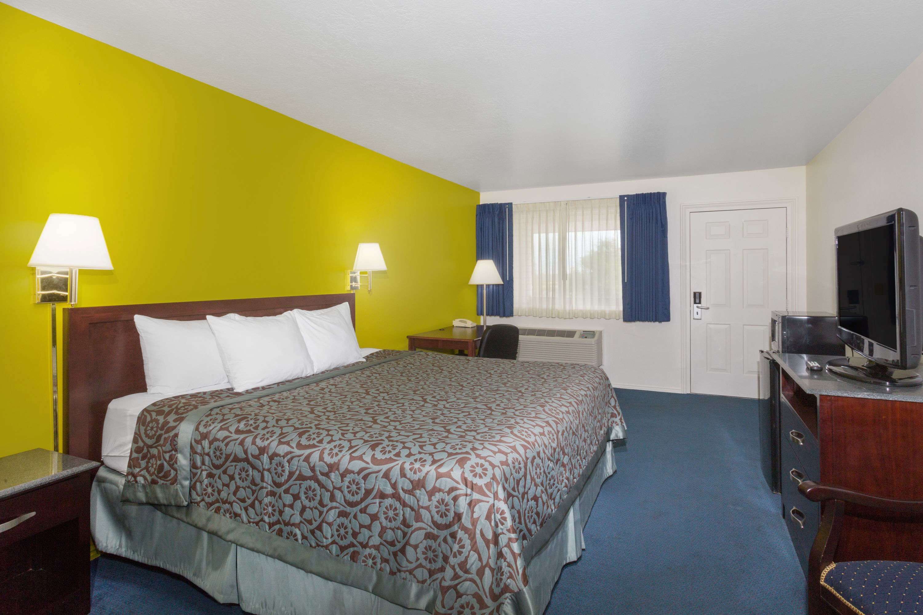A hotel room with a bed, two bedside lamps, a television, a desk, and a chair.