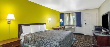 A hotel room with a bed, bedside lamps, a desk with a television, and a patterned carpet.