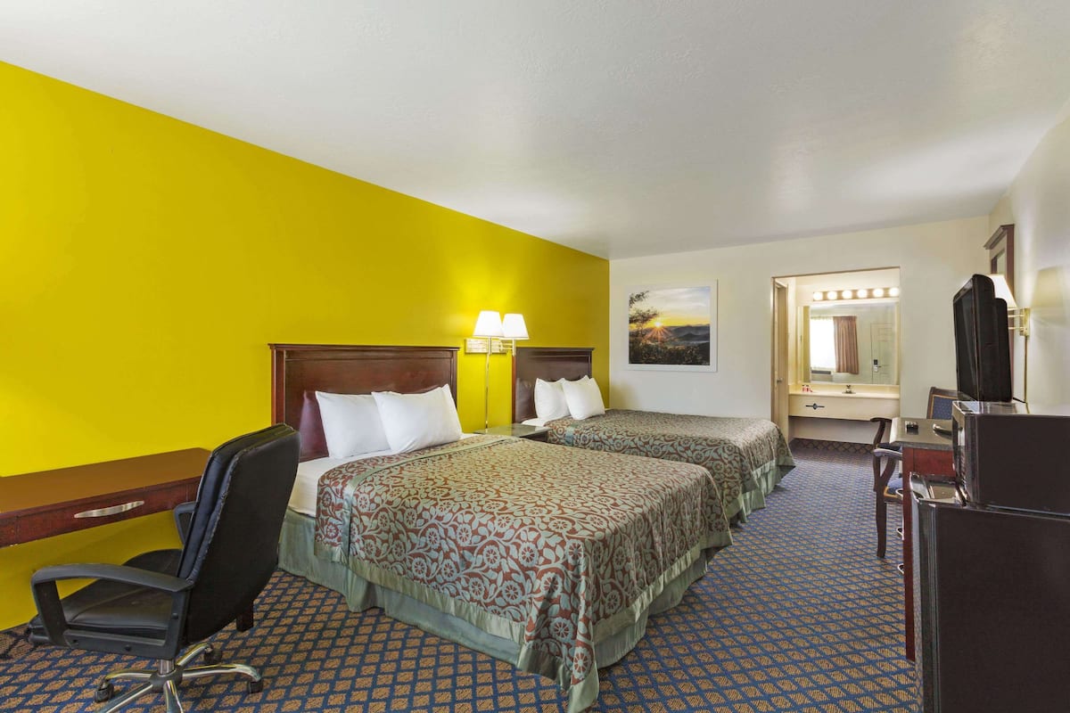 A hotel room with two beds, a desk, a chair, and a television.