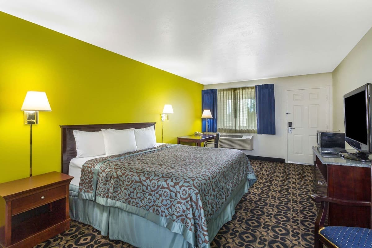 A hotel room with a bed, bedside lamps, a desk with a chair, a television, and a door.