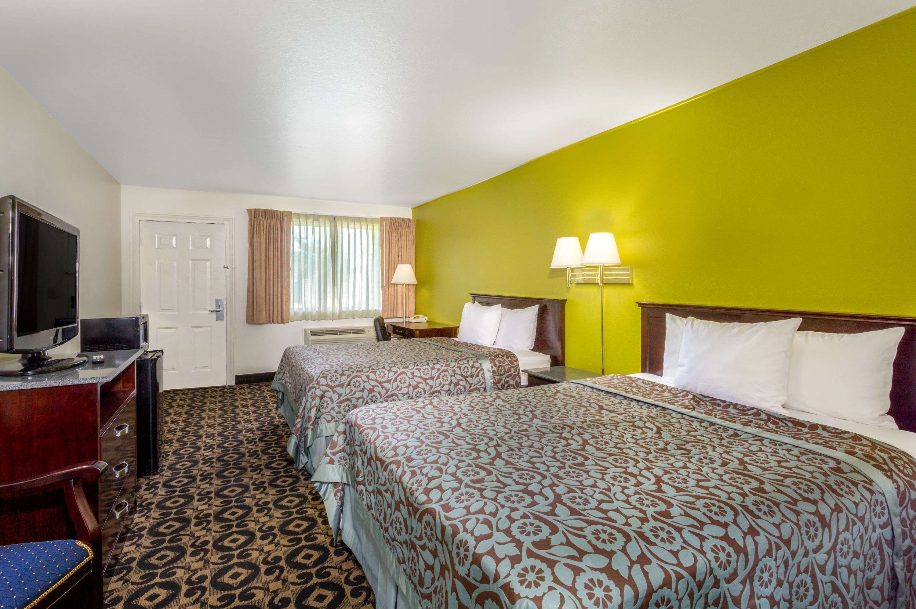 A hotel room with two beds, a TV, a desk, and a window with curtains.