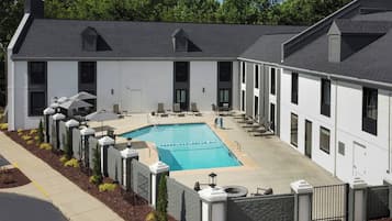 A modern building with a swimming pool, outdoor seating, and a gated entrance.
