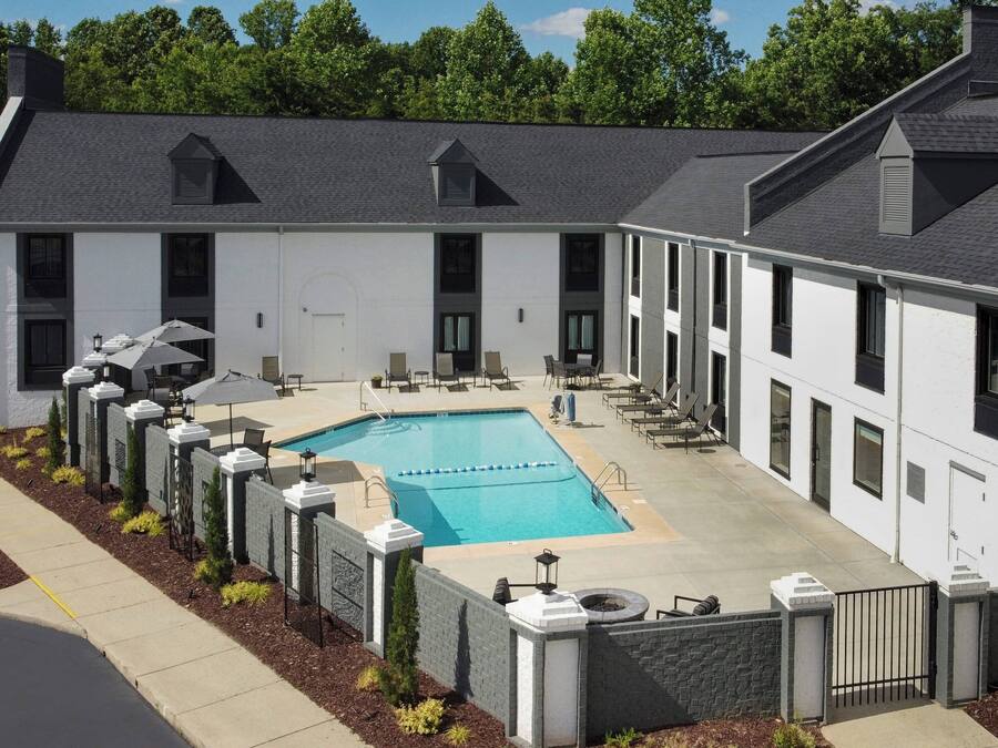 A modern building with a swimming pool, outdoor seating, and a gated entrance.