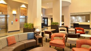 Eine Hotelhalle mit einer gebogenen Couch, mehreren Sesseln, einem runden Tisch und einer Rezeption.
