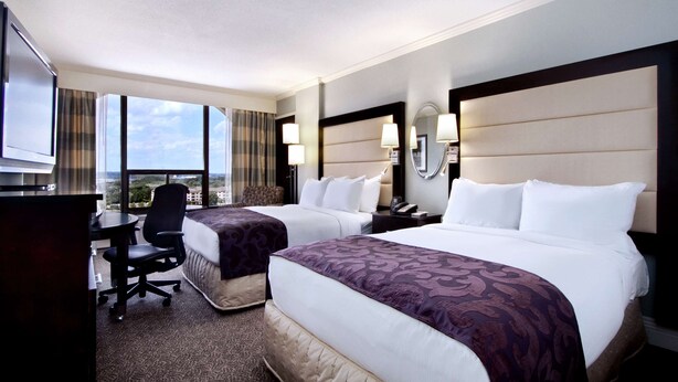 Ein Hotelzimmer mit zwei Betten, einem Schreibtisch, einem Sessel, einem Fernseher und einem großen Fenster mit Blick.