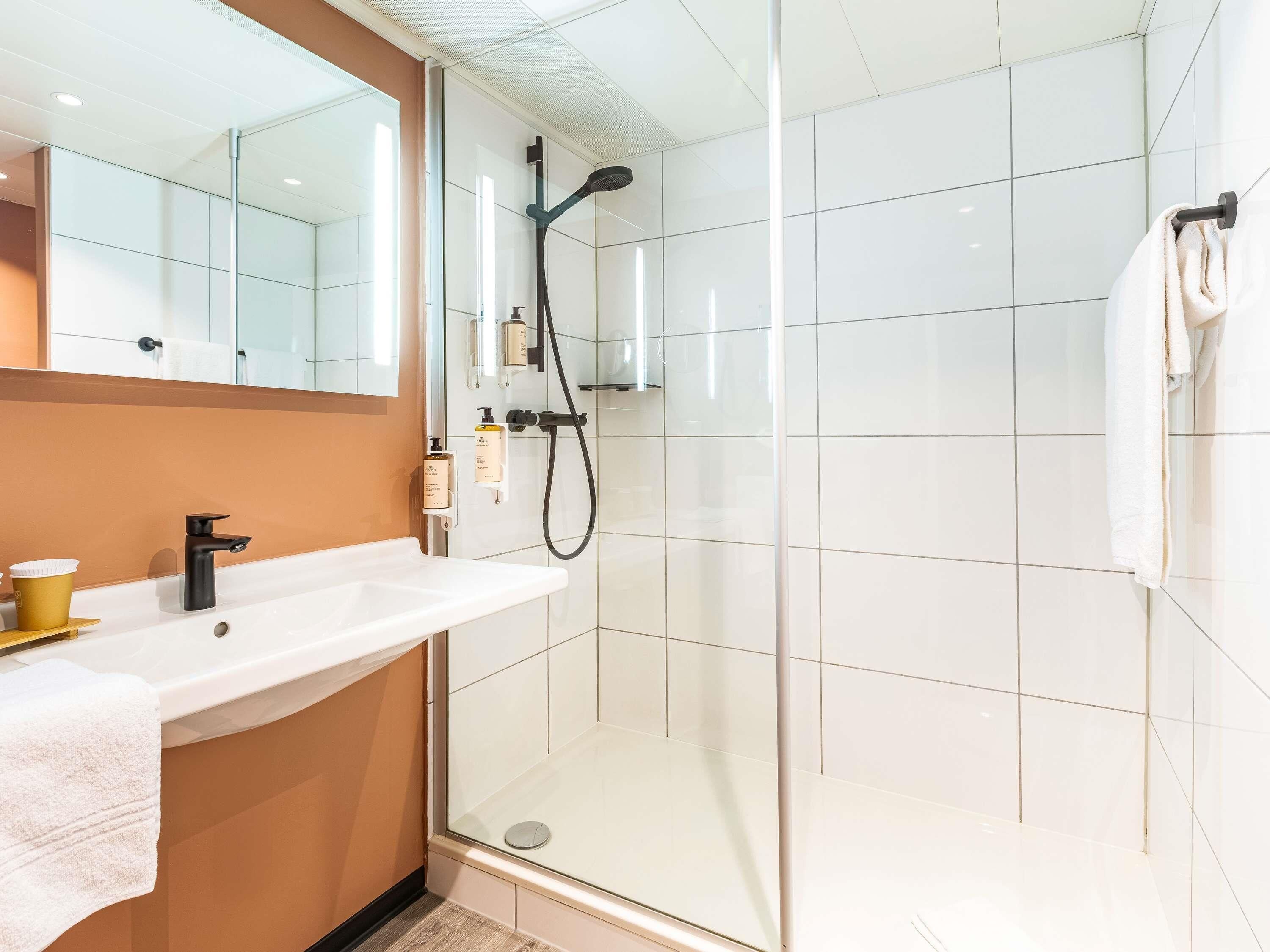 A modern bathroom with a glass shower enclosure, a white sink with a gold cup, and a towel rack.