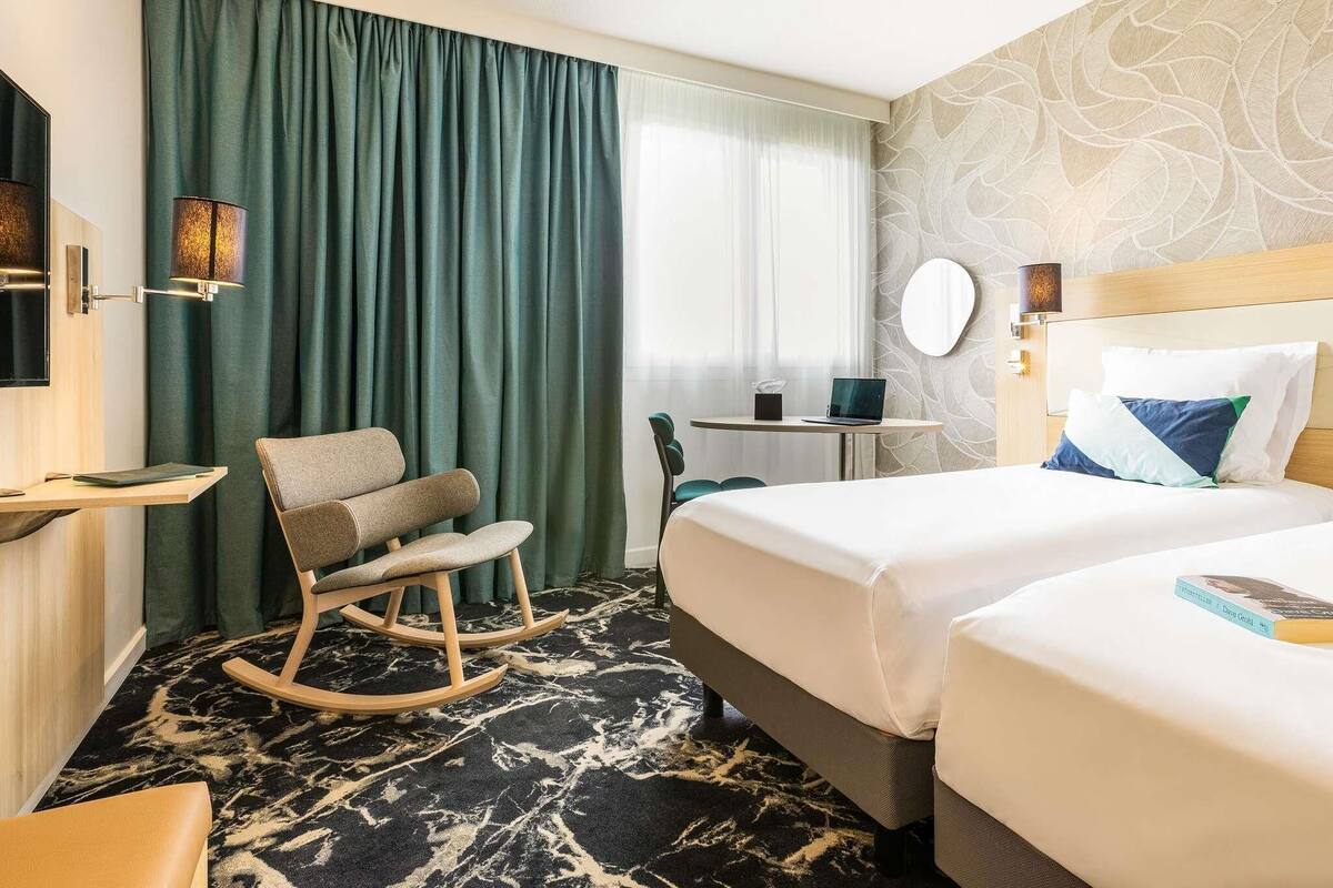 A hotel room with a bed, a desk, a chair, and a window with curtains.