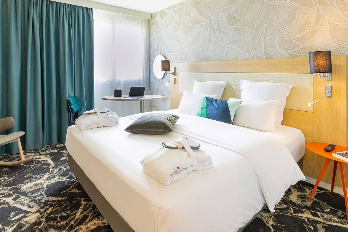 Una habitación de hotel con una cama, un escritorio con una computadora portátil, una silla y una pequeña mesa con un teléfono.