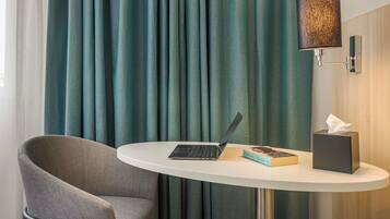 Habitación de hotel con cortinas azul verdoso, una computadora portátil sobre una mesita, un libro y una caja de pañuelos.