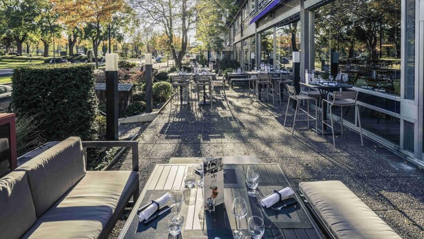 An outdoor dining area with tables and chairs, surrounded by trees and a building.