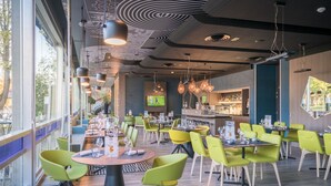 A modern restaurant with green chairs, a bar area, and a large TV screen.