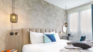 A hotel room with a large bed, a bedside table with a remote control, a small table with a book, and a mirror on the wall.