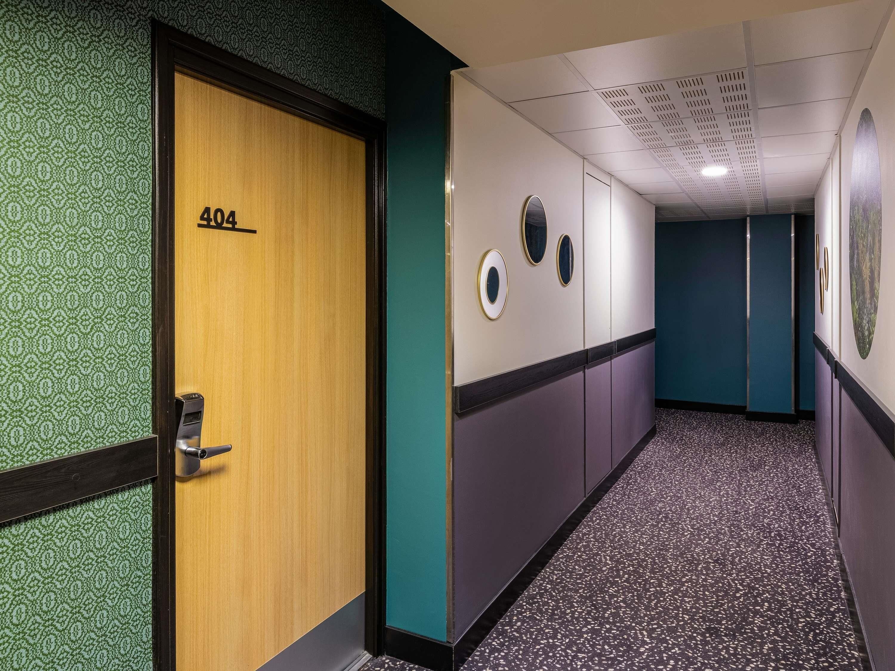 Um corredor com uma porta identificada como '404' e uma parede com espelhos redondos.