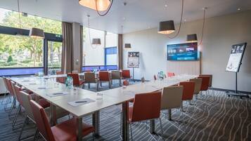 A conference room with a long table, red chairs, and a large screen on the wall.