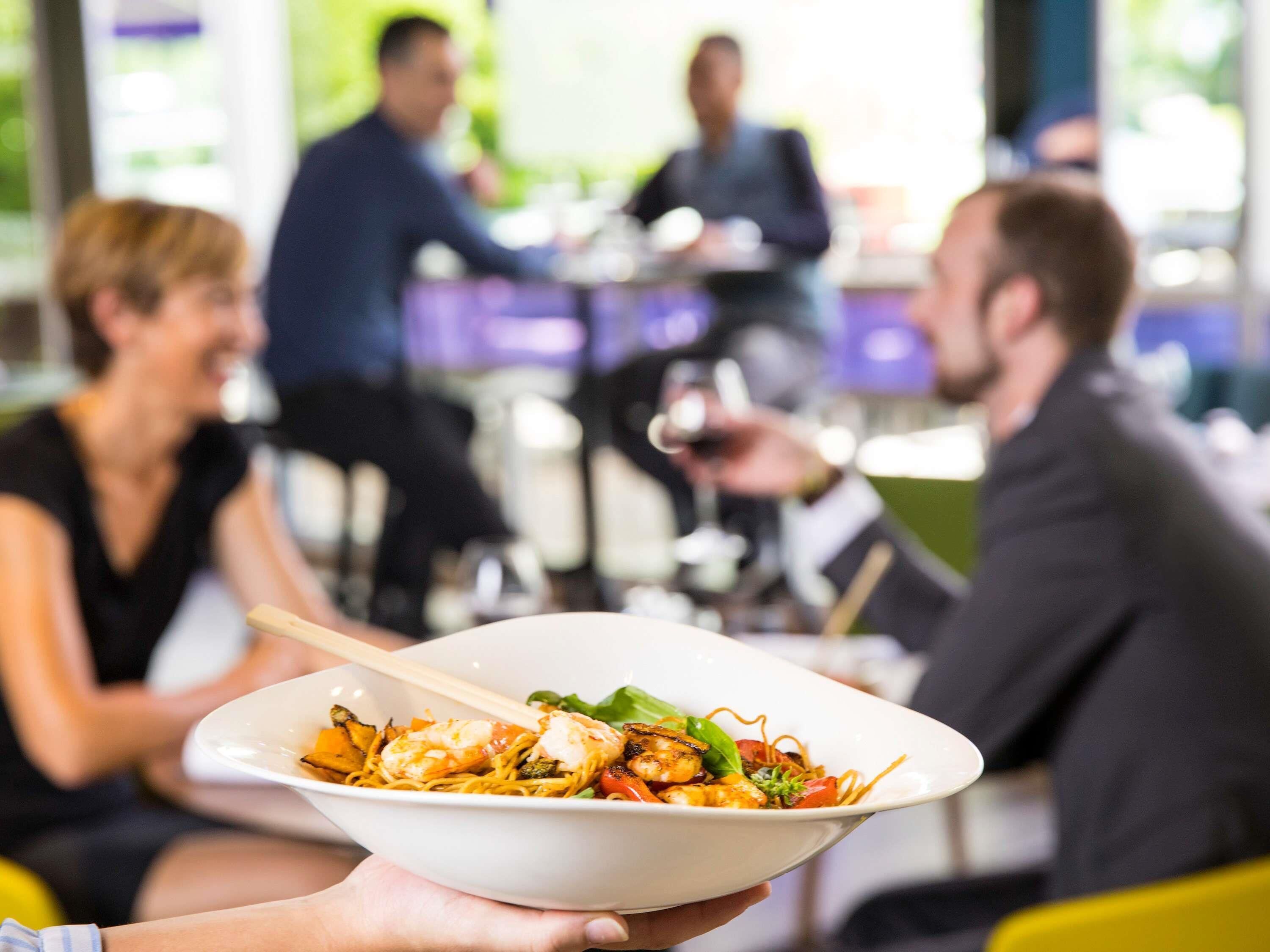 A person holding a bowl of food with a plate of food in the foreground.